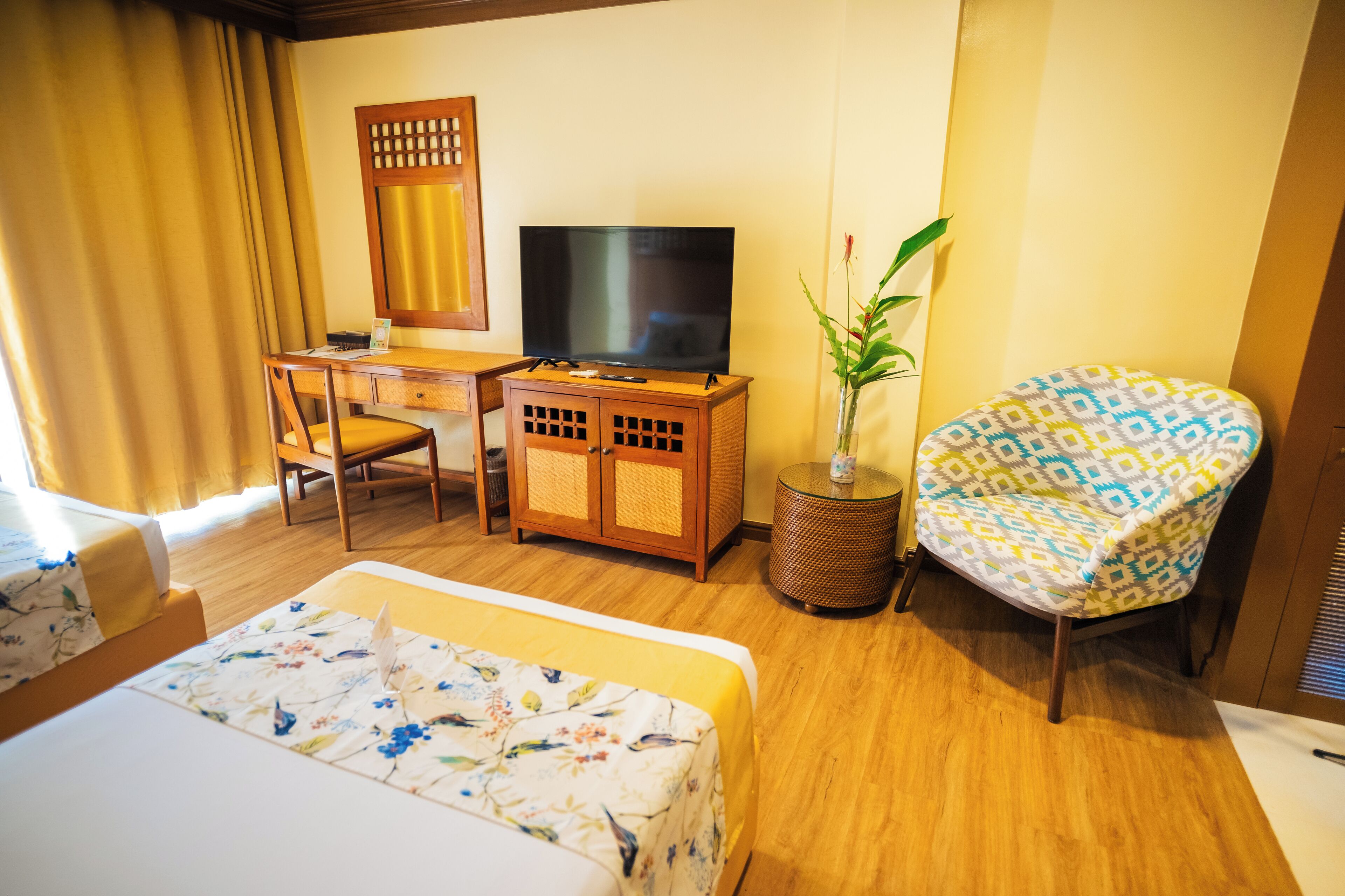 A hotel room with a bed, a desk with a TV, a chair, and a potted plant.
