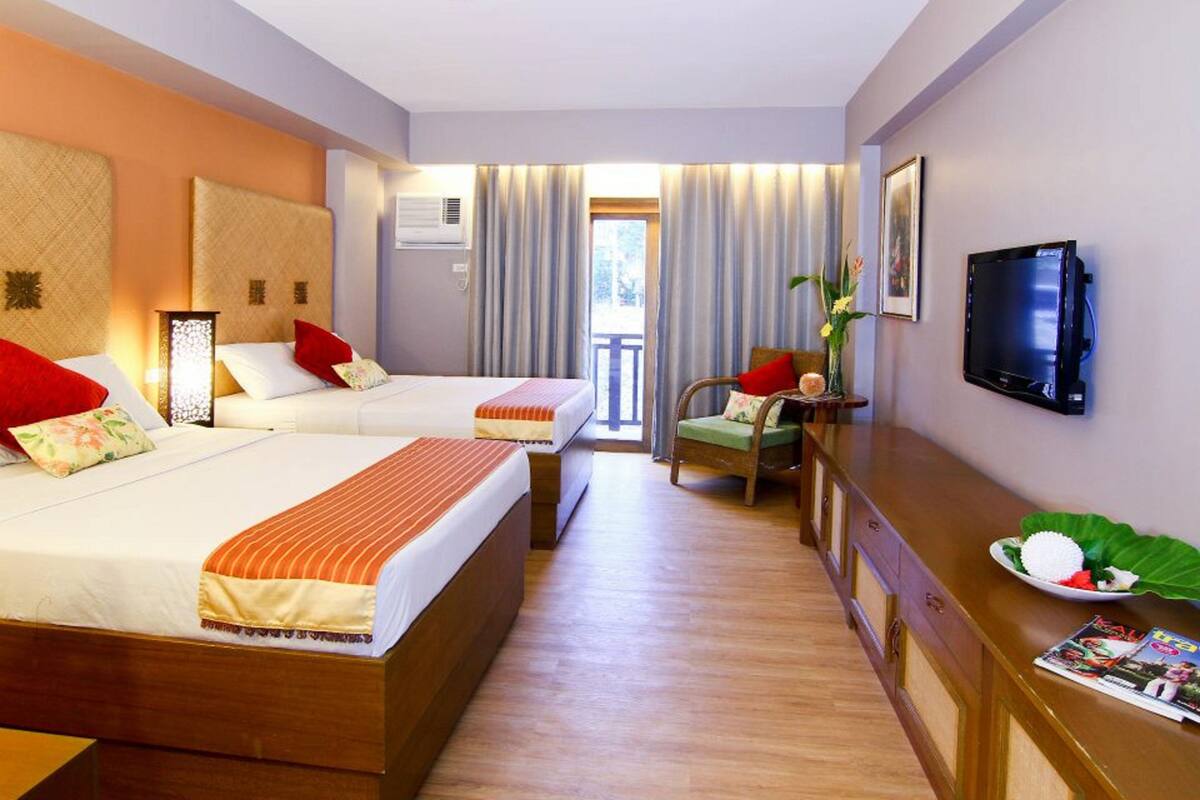 Habitación de hotel con dos camas, televisión, escritorio y vistas al exterior.
