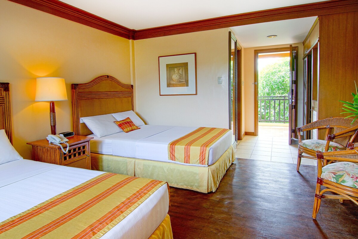 Une chambre d’hôtel avec deux lits, une table de chevet avec un téléphone, une chaise et une porte-fenêtre donnant sur un balcon.
