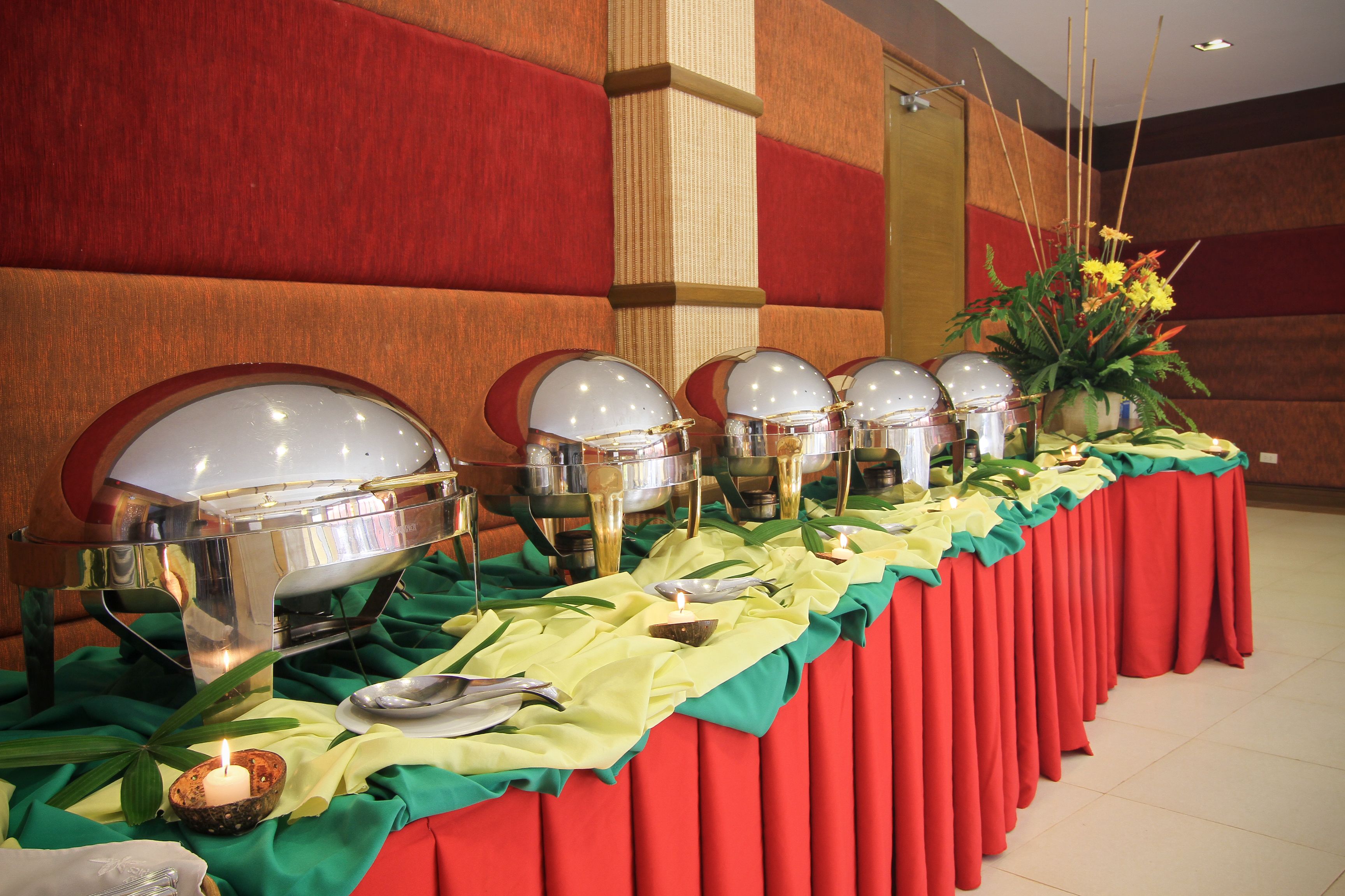 Montaje de bufé con varias estaciones de servicio, un arreglo floral central y un mantel verde.