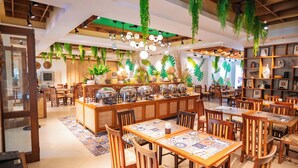 A restaurant with wooden tables and chairs, hanging plants, and a central bar area with food displays. - Boracay Tropics Resort Hotel (Boracay Island)