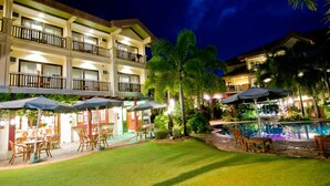 A hotel courtyard with outdoor seating, a swimming pool, and a well-lit building facade. - Boracay Tropics Resort Hotel (Boracay Island)