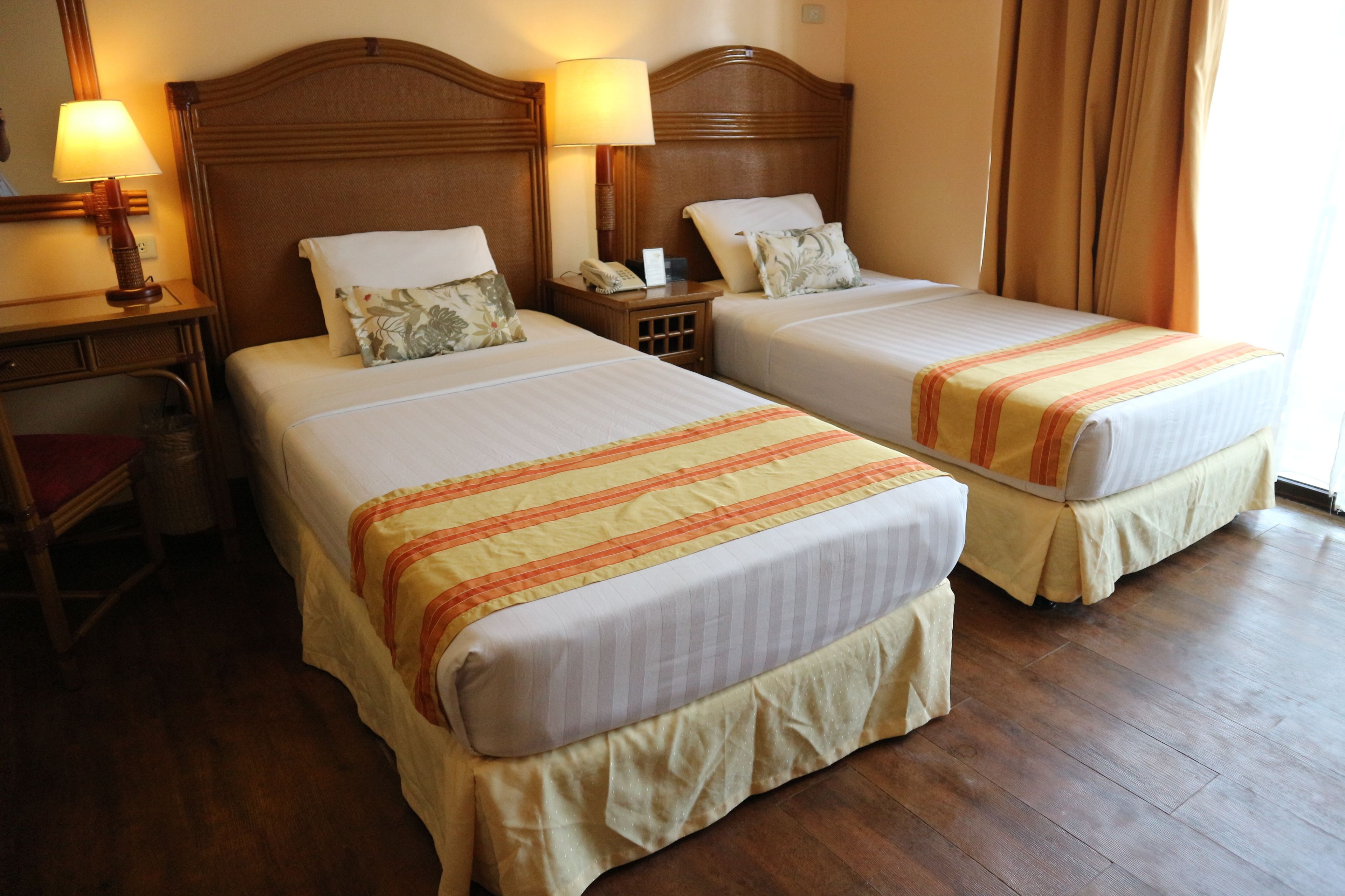 A hotel room with two beds, wooden headboards, bedside lamps, and a wooden floor.