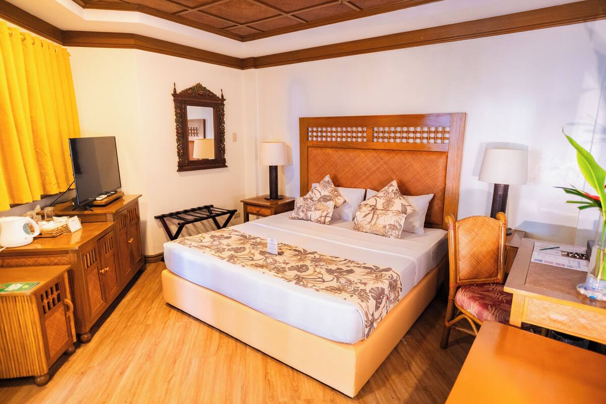 Una habitación de hotel con una cama grande, cabecera de madera, mesitas de noche con lámparas, un escritorio y un televisor.