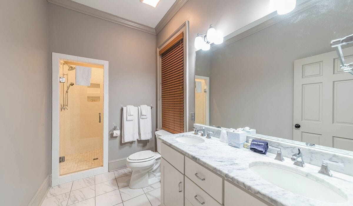 Un baño moderno con ducha a ras de suelo, inodoro, lavabo con un espejo grande y tocador con cajones.