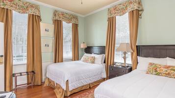 A hotel room with two beds, a nightstand, a lamp, and a window with curtains.
