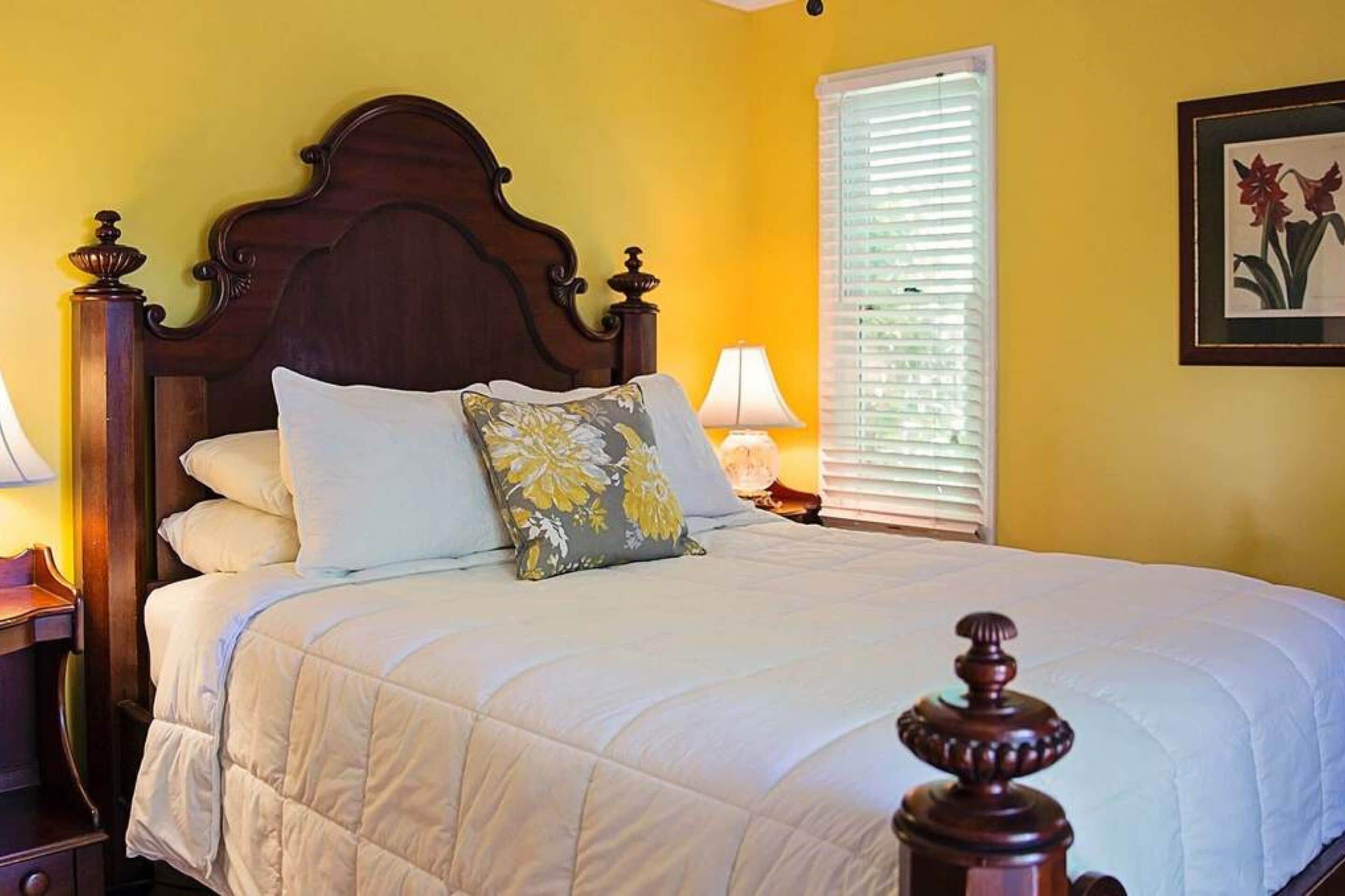 A neatly made bed with a wooden headboard, a floral pillow, and a bedside lamp.