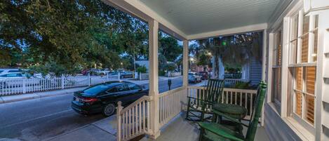 A porch with a white railing, green chairs, and a black car parked on the street.