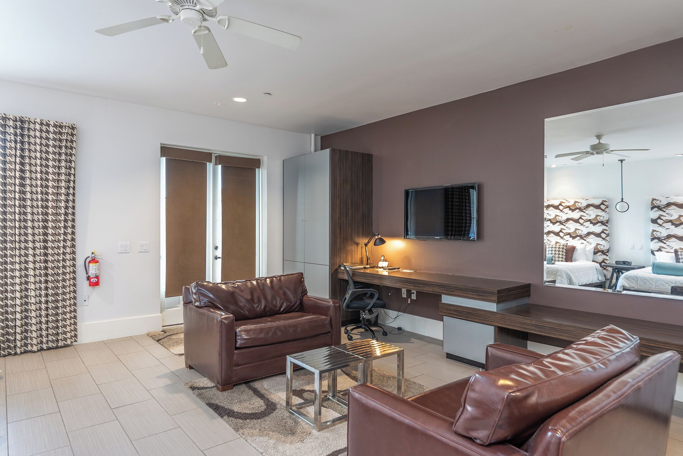A modern living room with leather sofas, a coffee table, a desk with a computer, and a TV mounted on the wall.