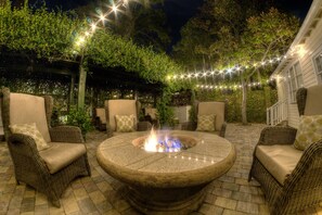 An outdoor patio with wicker furniture, a central fire pit, and string lights.