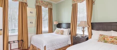 A hotel room with two beds, a nightstand with a lamp, a small table, and a window with curtains.