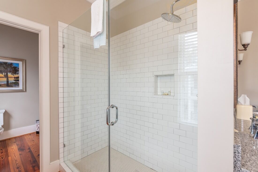 Una ducha con paredes de vidrio y azulejos blancos, una puerta de cristal y un cabezal de ducha.