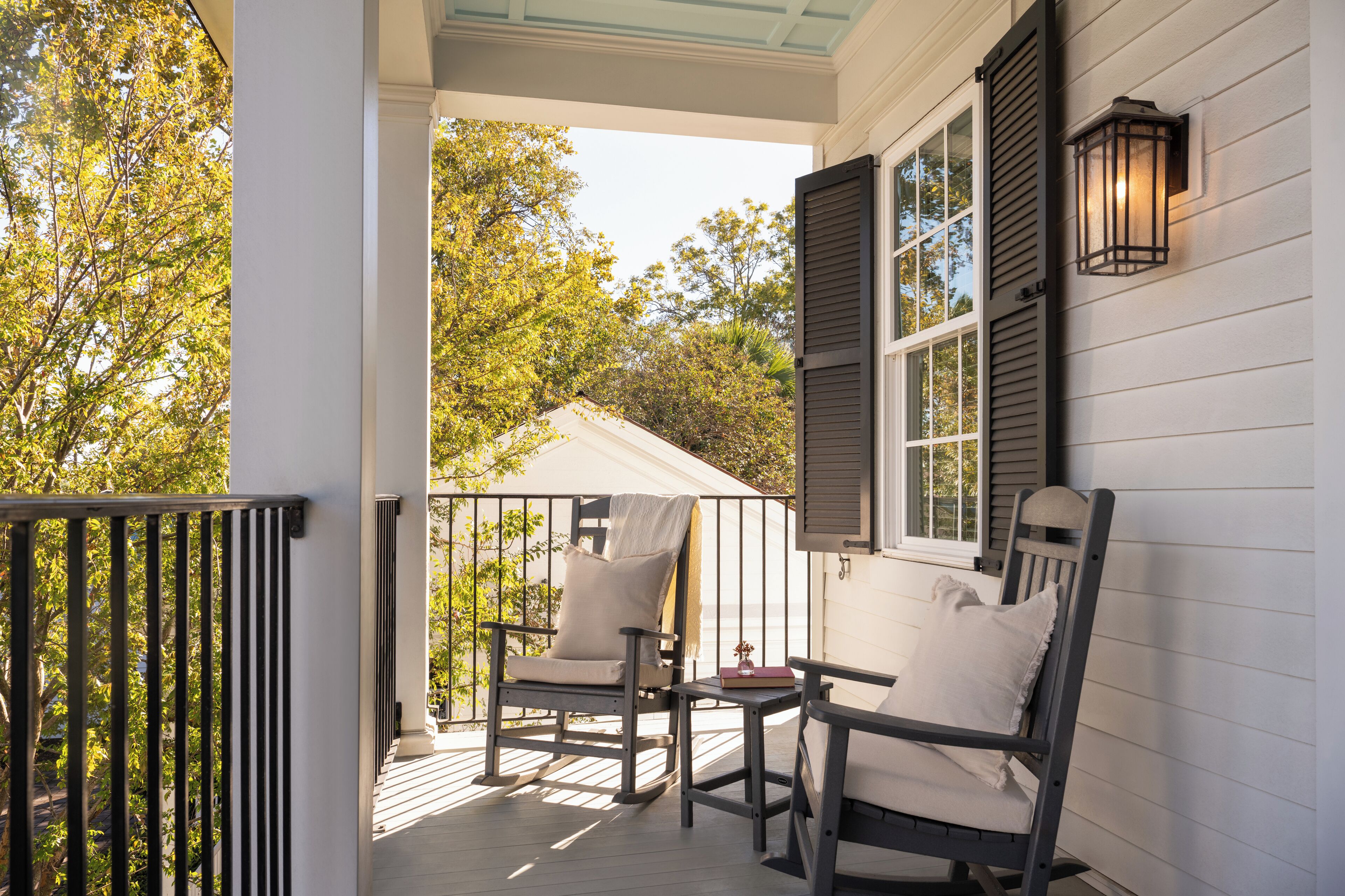 A porch with two rocking chairs and a small table, overlooking a tree-lined street.