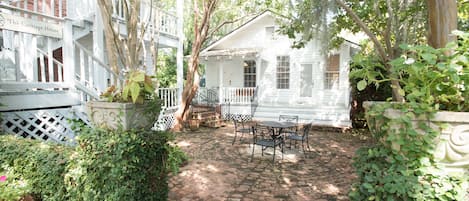 A white house with a porch, surrounded by greenery and a brick pathway.