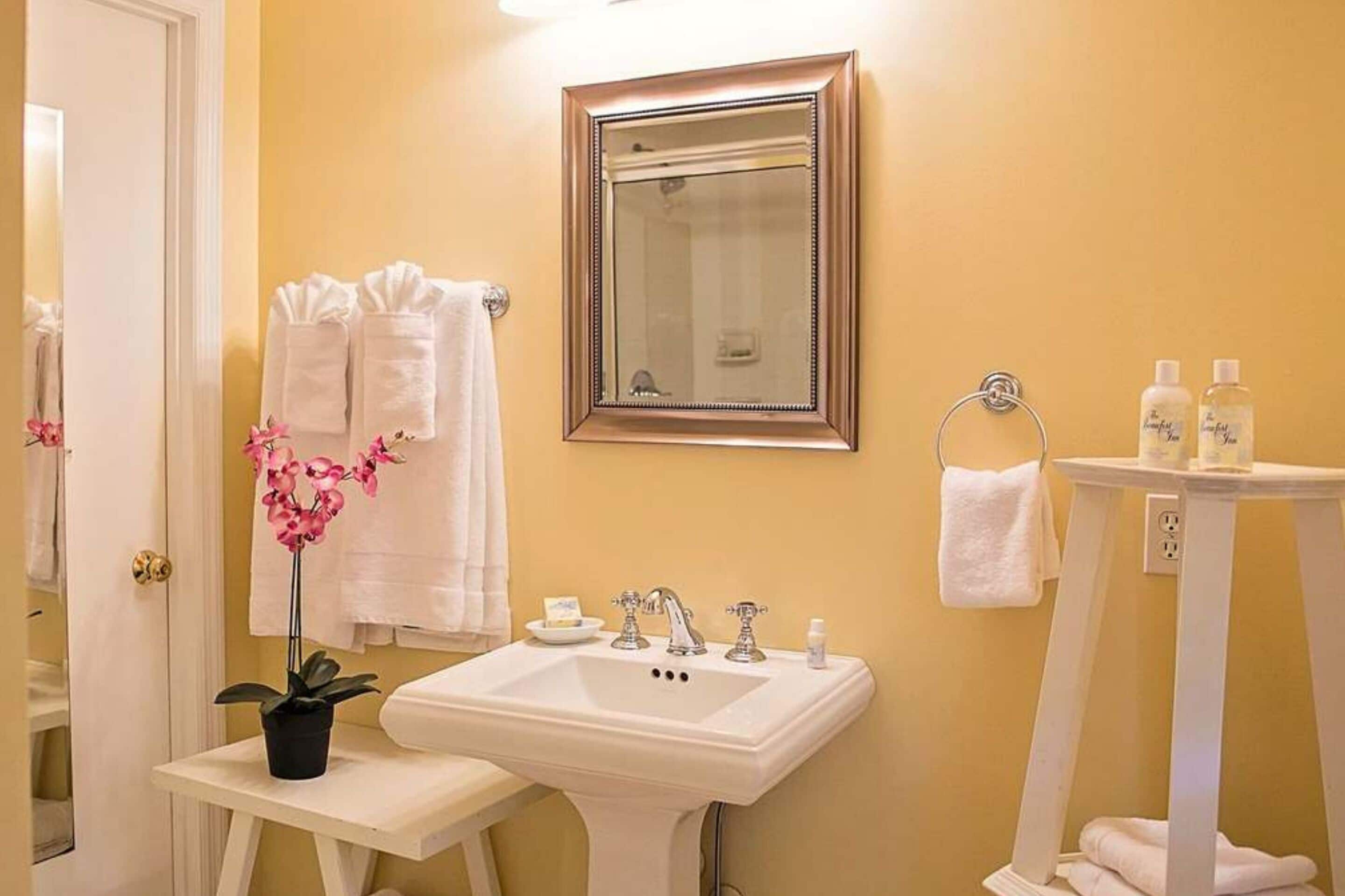 A bathroom with a white sink, a mirror, and a small table with a potted orchid.
