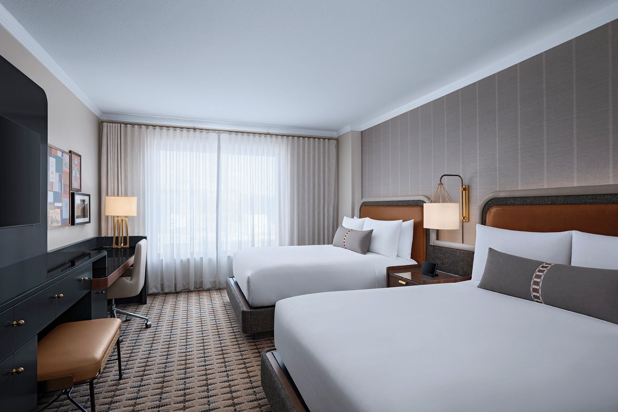 A hotel room with two beds, a desk, a chair, a lamp, and a carpeted floor.