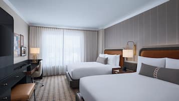 A hotel room with two beds, a desk, a chair, a lamp, and a carpeted floor.