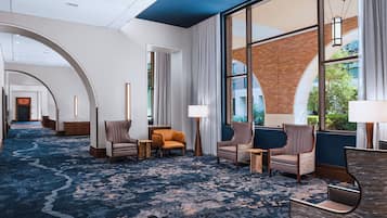 A hotel lobby with a blue carpet, seating area with chairs, a reception desk, and large windows offering views of the outside.