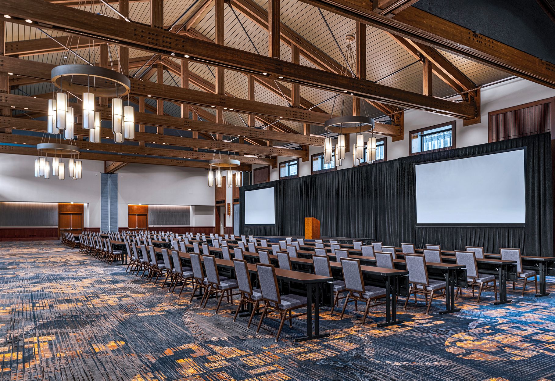 A conference room with rows of chairs, a large screen, and a high ceiling with exposed beams.