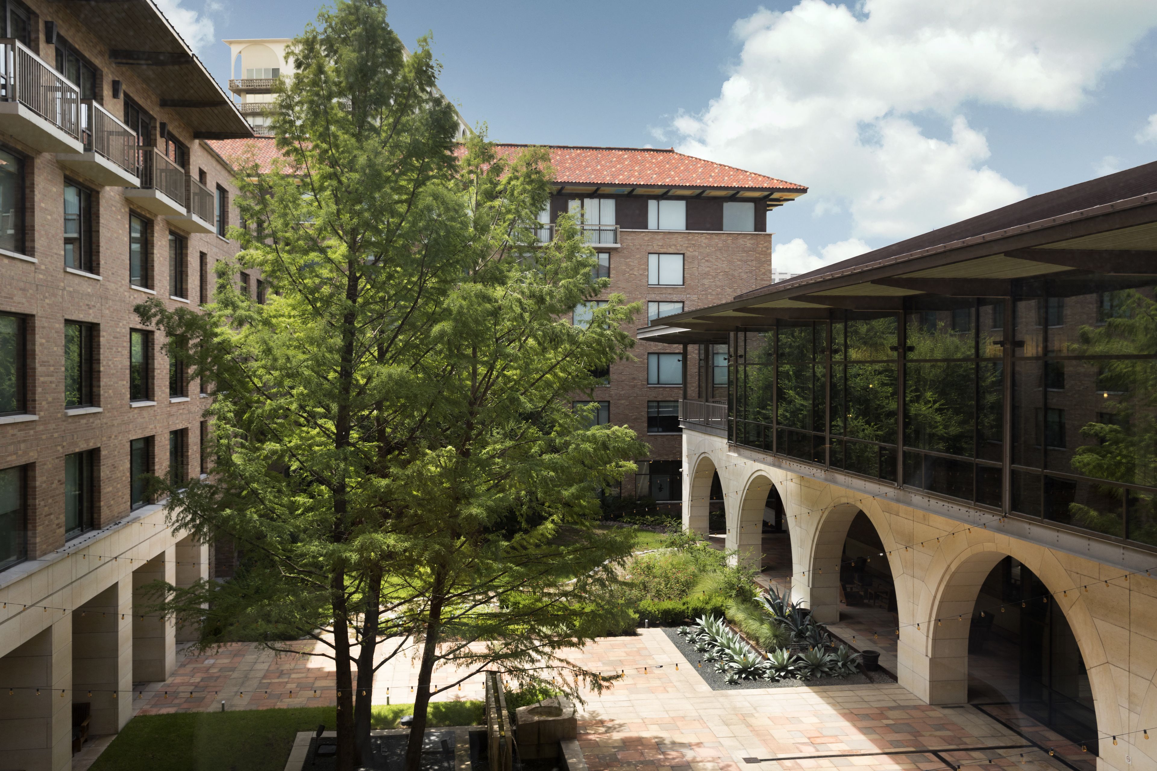 A courtyard with a central tree, brick buildings, and a covered walkway with arches.