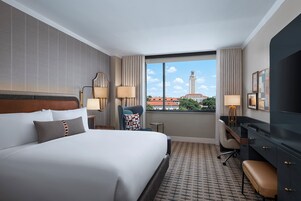 Habitación de hotel con una cama grande, un escritorio, una silla y vista a un paisaje urbano.