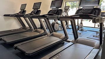 A row of treadmills with digital screens, a stationary bike, and a rowing machine in a gym.