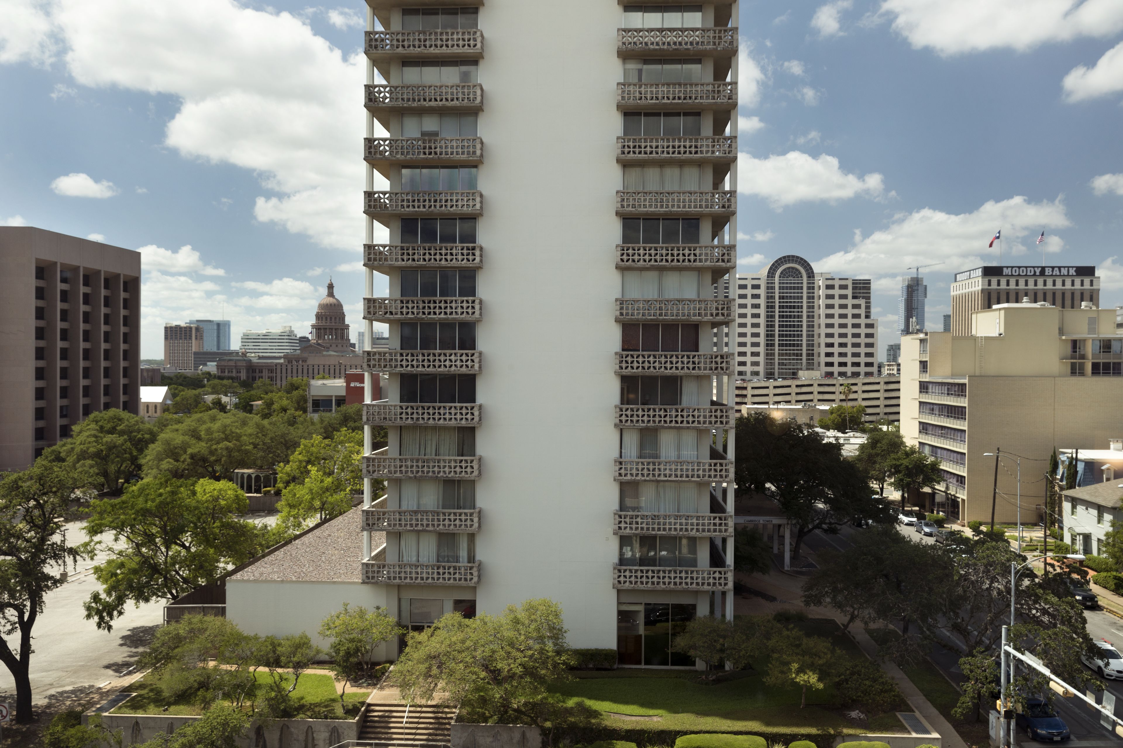 Um edifício de vários andares com varandas, rodeado por árvores e outros edifícios.