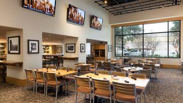 A spacious dining area with multiple tables and chairs, framed pictures on the walls, and large windows offering a view of the outside.
