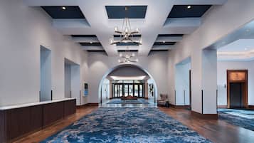 Un'ampia galleria con tappeto a motivi blu, un lampadario al centro e vista su uno spazio esterno attraverso un arco.