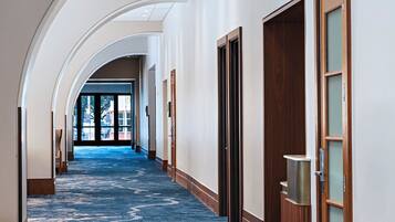 A hotel corridor with a blue carpet, wooden doors, and a skylight.