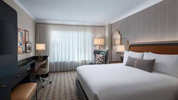 Una habitación de hotel con una cama grande, un escritorio, una silla, una lámpara y un ventanal con cortinas.