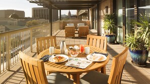 A balcony with wooden furniture, a table with breakfast items, and potted plants. - AT&T Hotel & Conference Center at the University of Texas (Austin)