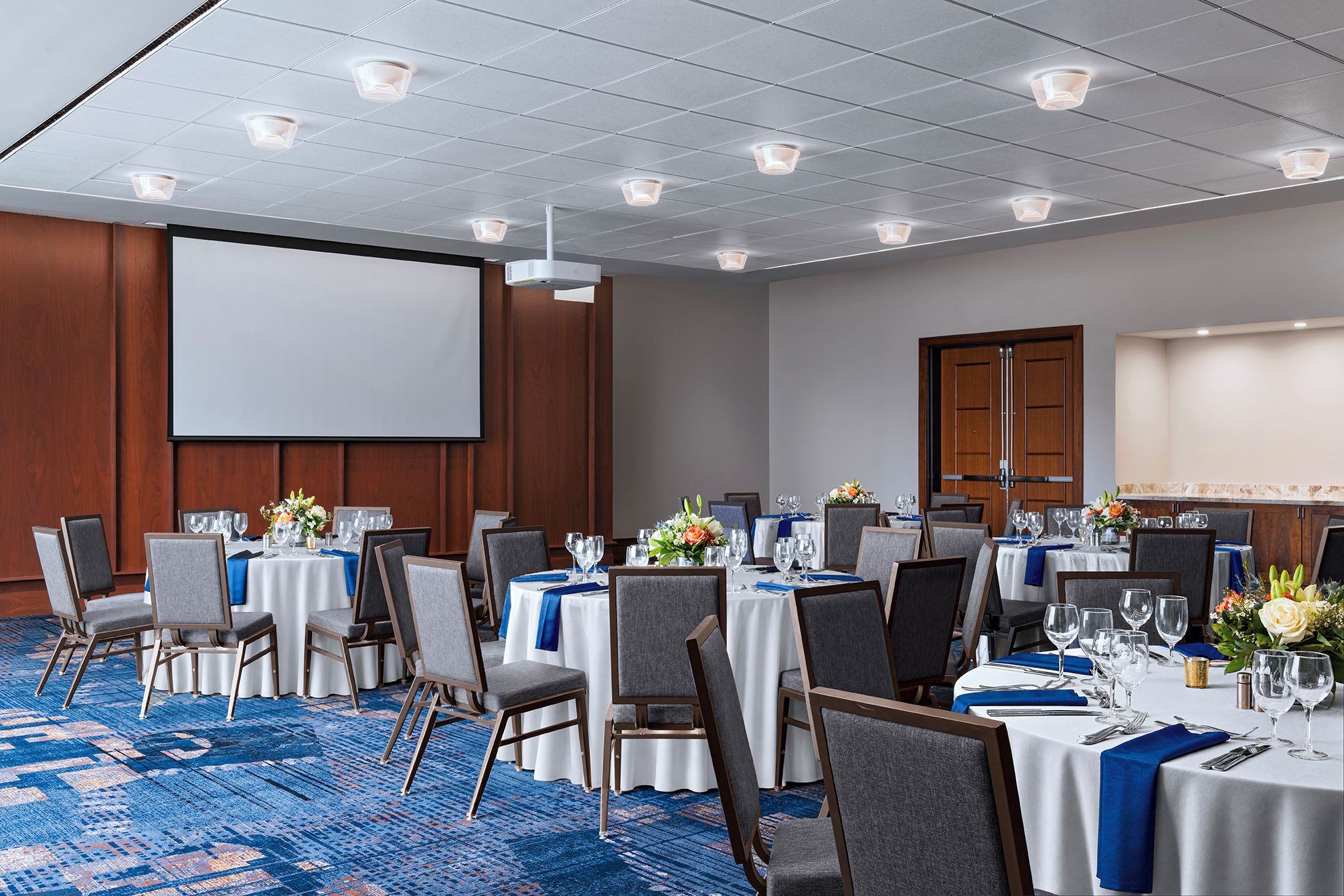 A conference room with multiple tables, chairs, a projector screen, and a large screen.