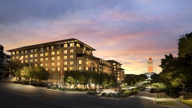 A multi-story hotel with a modern design, featuring a prominent tower in the background. - AT&T Hotel & Conference Center at the University of Texas (Austin)