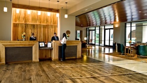 A reception area with wooden reception desks, a large window, and a modern interior design. - AT&T Hotel & Conference Center at the University of Texas (Austin)