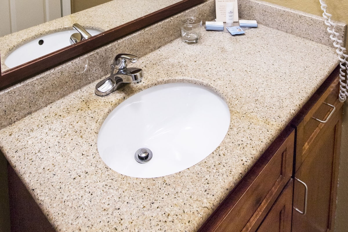 A bathroom with a granite countertop, a white sink, a mirror, and a hairdryer mounted on the wall.