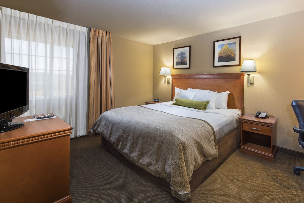 A hotel room with a large bed, a desk with a computer, a TV, and a chair.