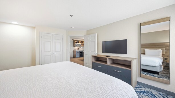 A hotel room with a large bed, a TV, a mirror, and a kitchenette in the background. - Candlewood Suites Macon by IHG (Macon)