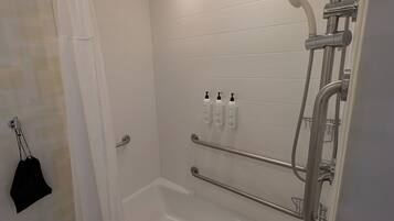 A modern bathroom with a bathtub, shower, and handrails.