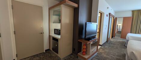 Habitación de hotel con un televisor sobre un soporte de madera, un microondas en un estante y un minibar.
