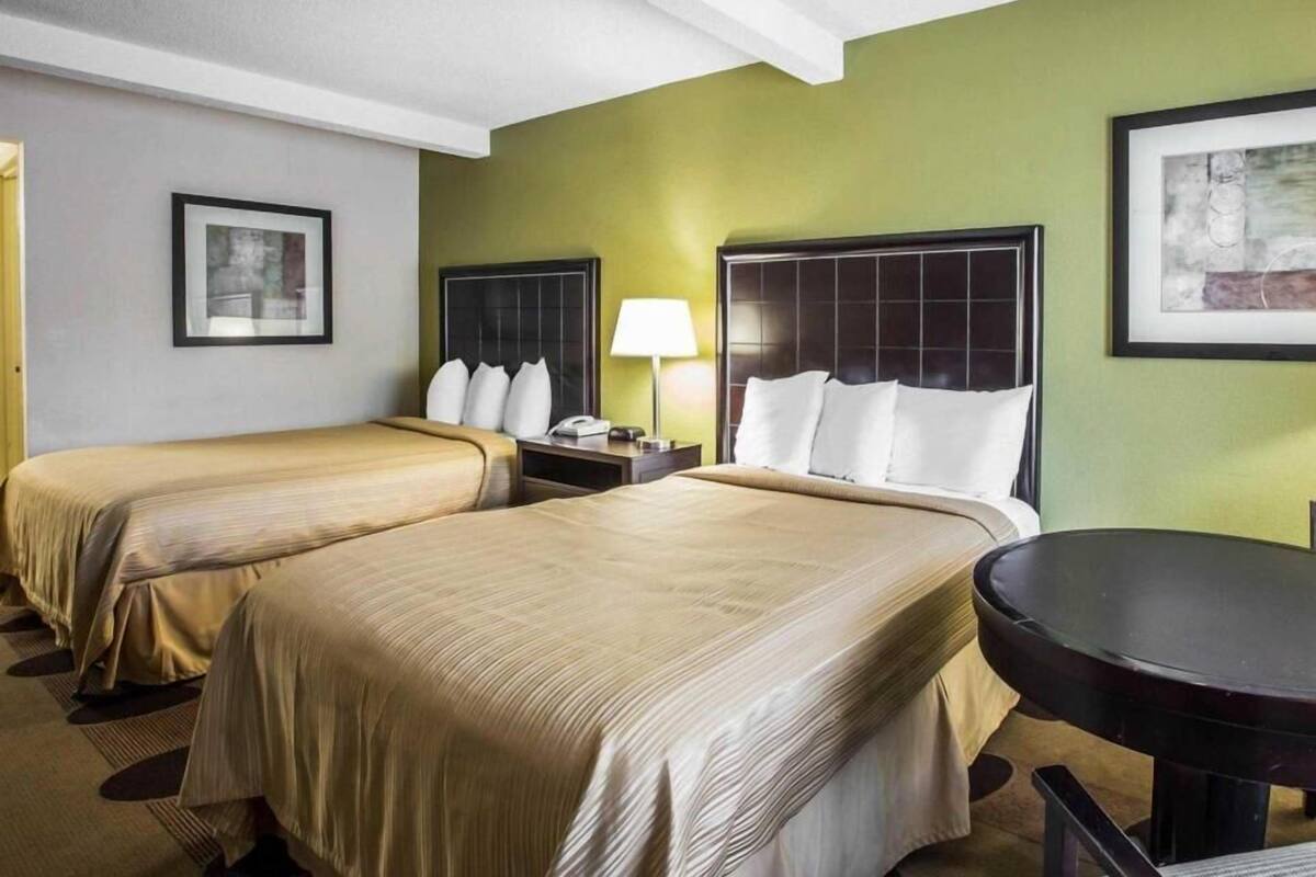 A hotel room with two beds, a nightstand, a lamp, and a round table.