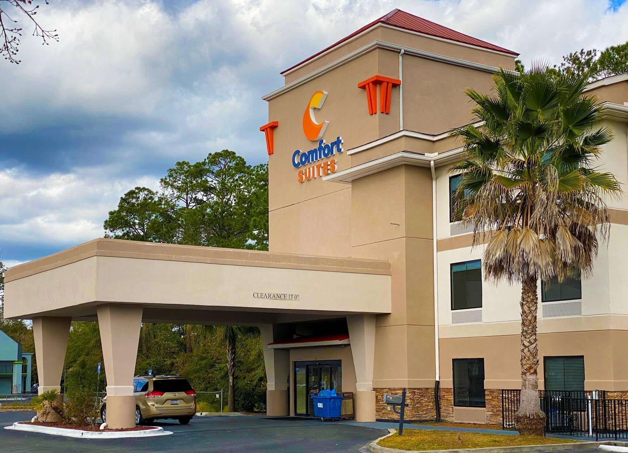 Un hotel Comfort Suites con entrada techada, palmeras y cielo despejado.