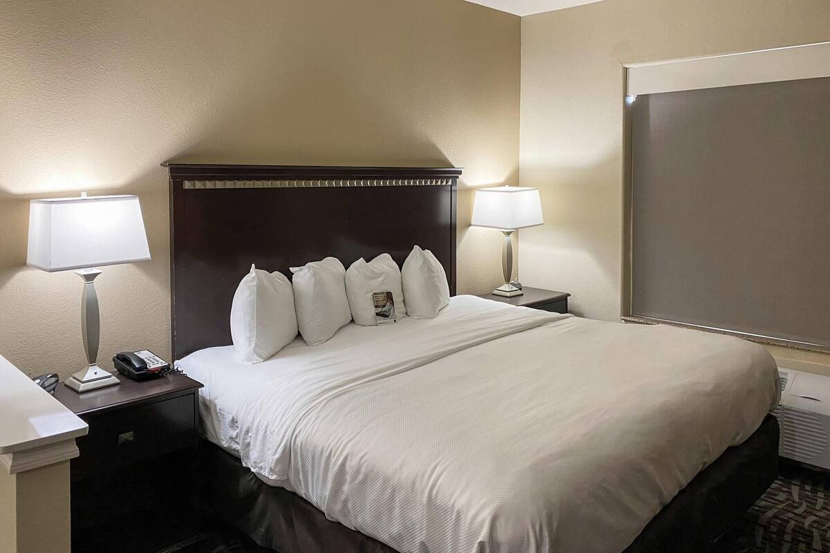 A hotel room with a large bed, two bedside tables with lamps, a telephone, and a window.