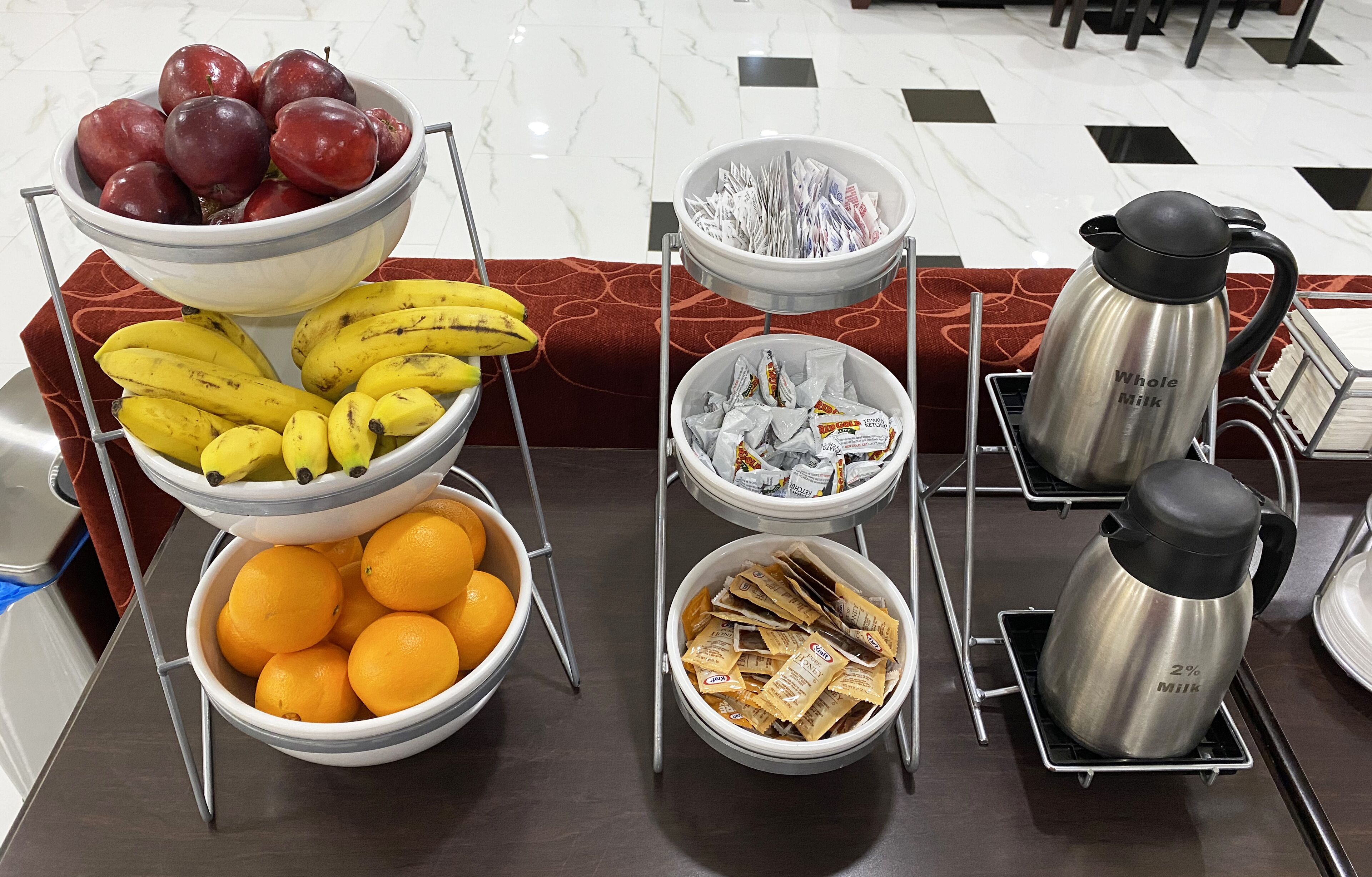 A breakfast buffet with fruits, bananas, oranges, and milk packets.