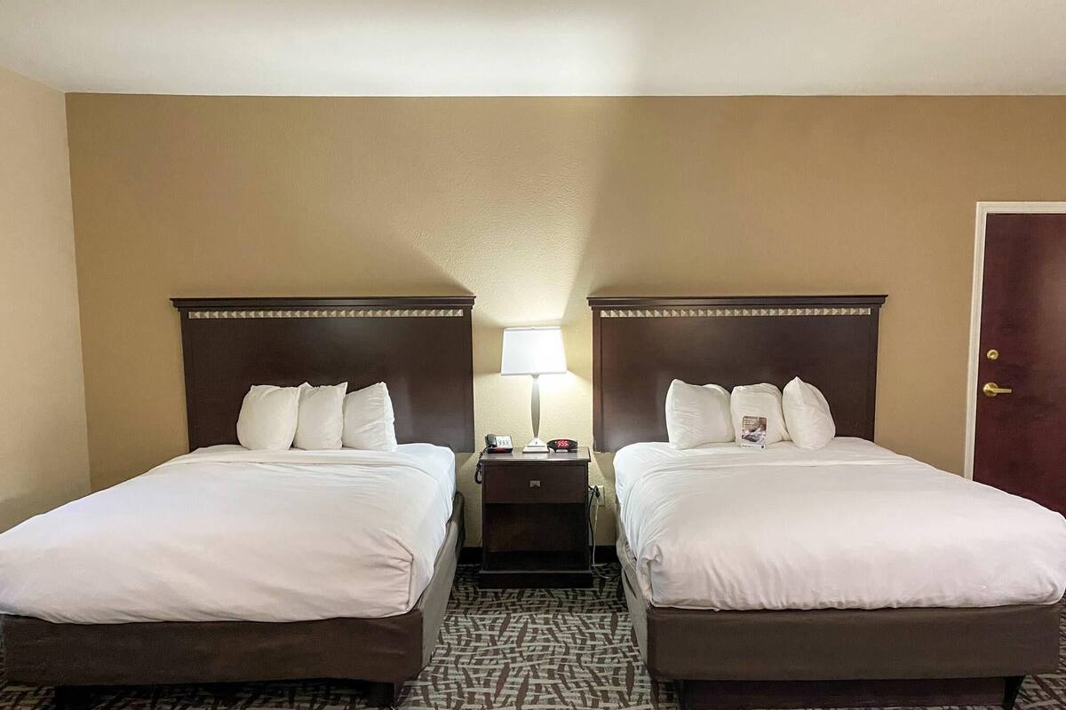 A hotel room with two beds, a nightstand with a lamp, and a door.