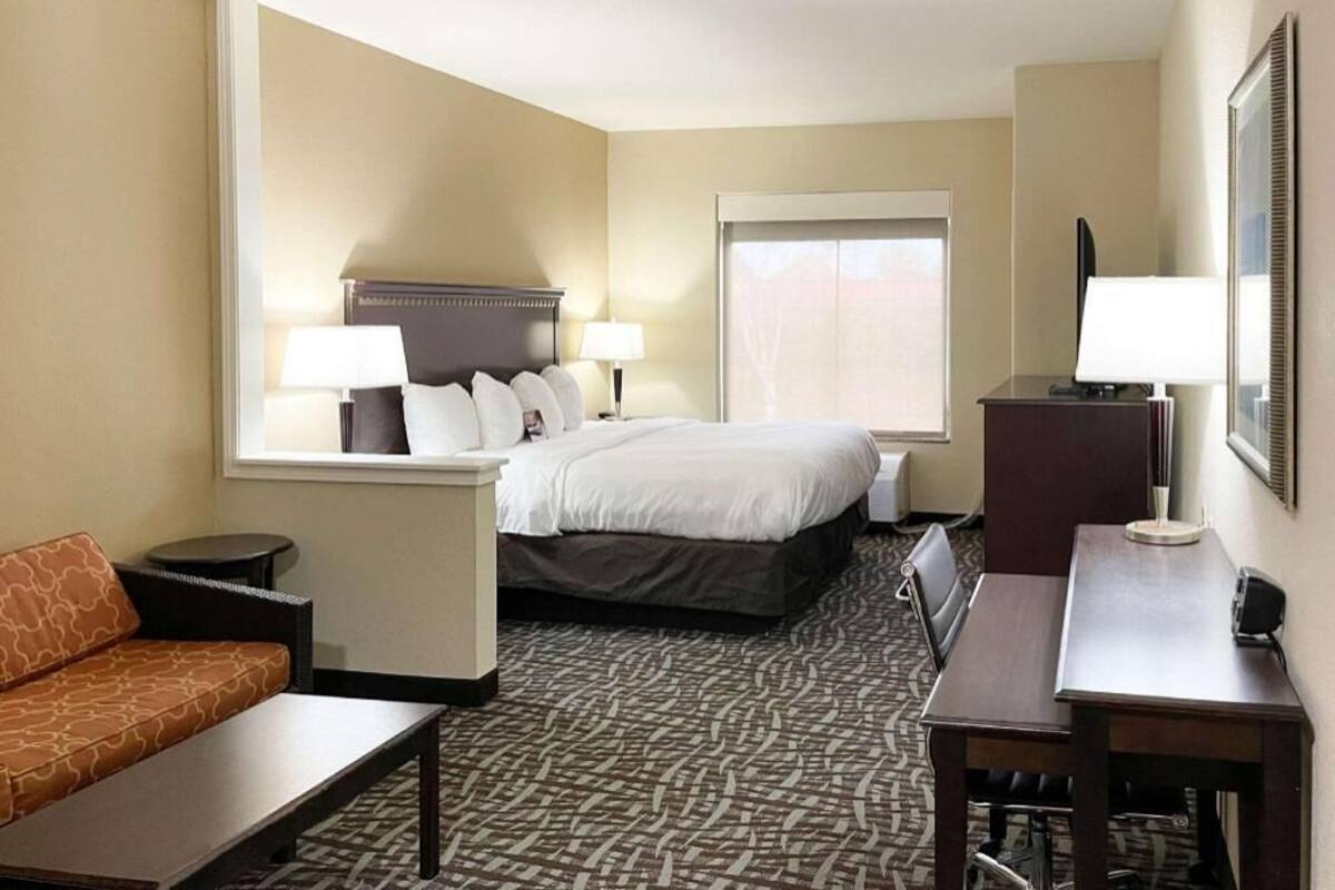 A hotel room with a bed, two bedside tables with lamps, a sofa, a desk, and a chair.
