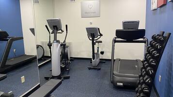 A gym with treadmills, elliptical machines, a stair climber, and a rack of dumbbells.