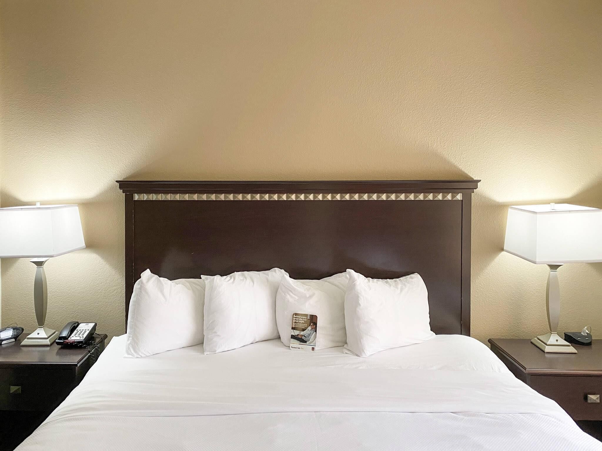 A hotel room with a large bed, two bedside tables, a nightstand, a lamp, and a telephone on the nightstand.