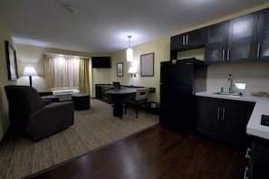 Un espacio habitable compacto con sofá, mesa de comedor, zona de cocina con armarios y un refrigerador, y una televisión pequeña en la pared.