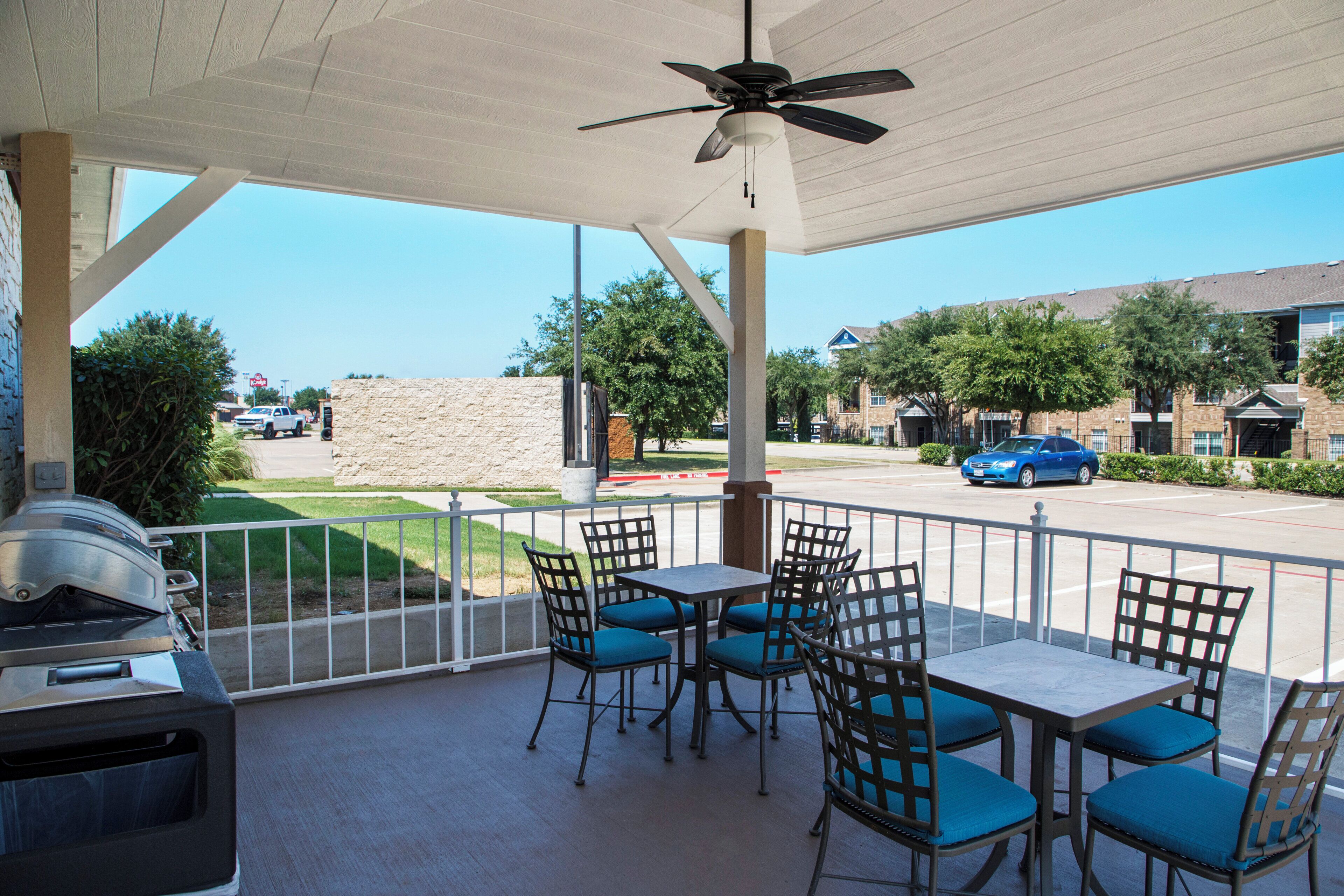 An outdoor patio with tables and chairs, a ceiling fan, and a grill.